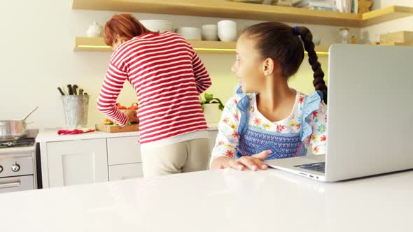 Mother and daughter using laptop in kitchen worktop 4k