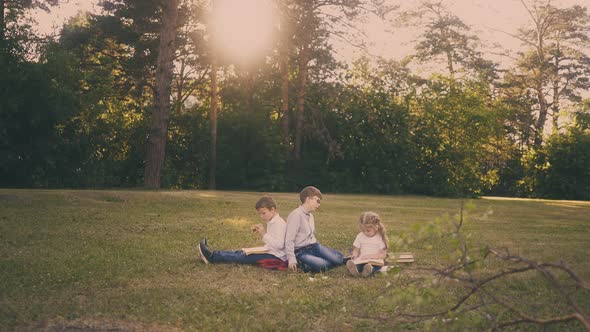 Schoolchildren Do Home Task with Sister Sitting on Lawn