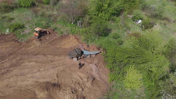 Aerial shot of tipper unloading ground on further construction site.