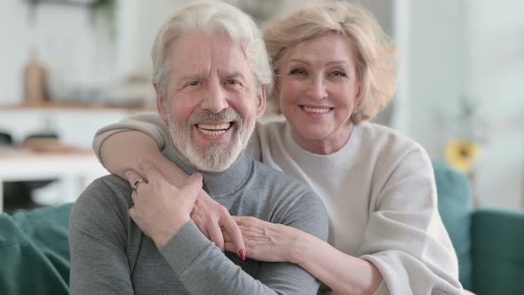 Embracing Old Couple Smiling at Camera While Sitting on Sofa