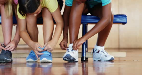 Girls tying shoe laces in basketball court