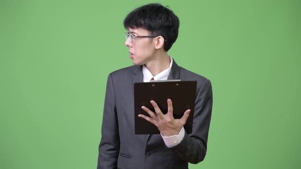 Young Asian Businessman Reading with Clipboard and Talking To the Side