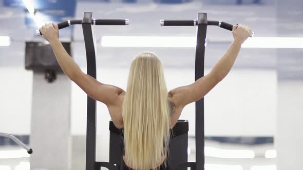 Strong Female Bodybuilder with Blond Hair with Muscular Arms Performing Pulls Up on a Horizontal Bar