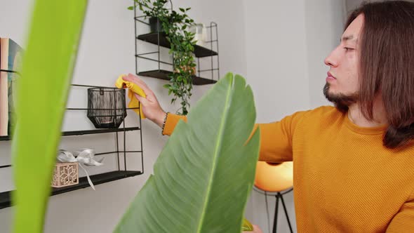 Caucasian Man with Long Brown Hair and Beard Wearing Orange Sweater Cleaning Metal Shelves in Room