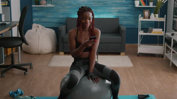 Slim Fit Black Woman Sitting on Fitness Ball Typing Message on Phone