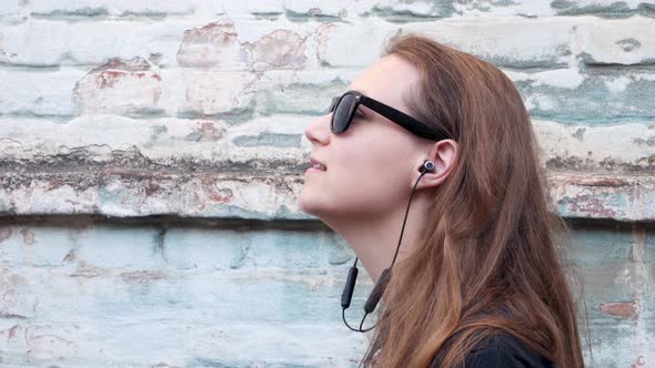 Young attractive girl in black t-shirt sunglasses in rock style on urban background listening music