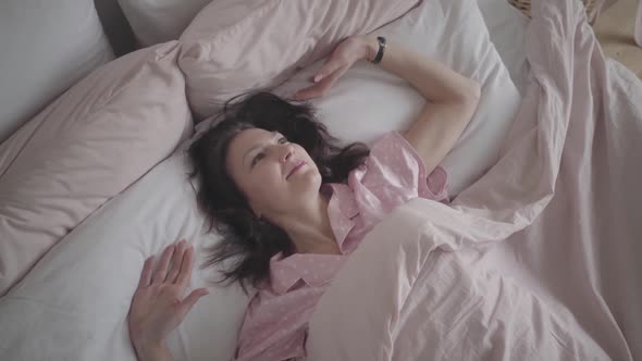 Top View of Positive Adult Caucasian Woman Stretching in Bed in the Morning and Smiling at Camera