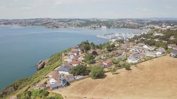 Drone ascending over the town in Torquay England. Homes, resorts, and hotels are visible in the dist