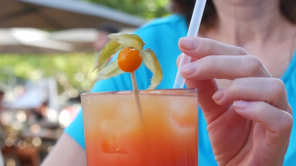 A Woman Holds a Cocktail Tube in Her Fingers