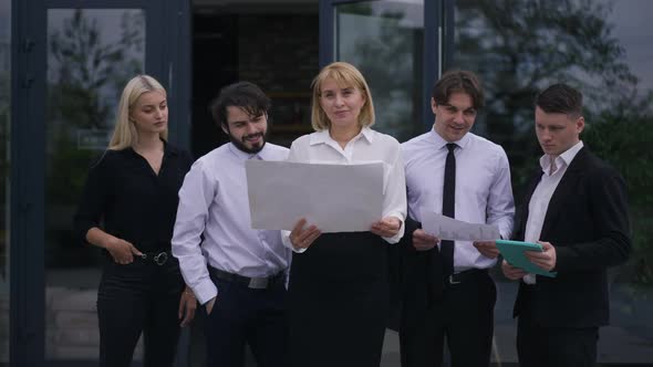 Front View Five Confident Caucasian Men and Women Analyzing Paperwork Standing on Office Terrace and