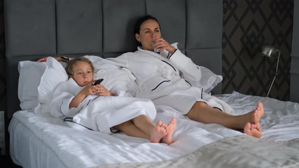 Woman with Little Daughter in Bathrobes Watch TV