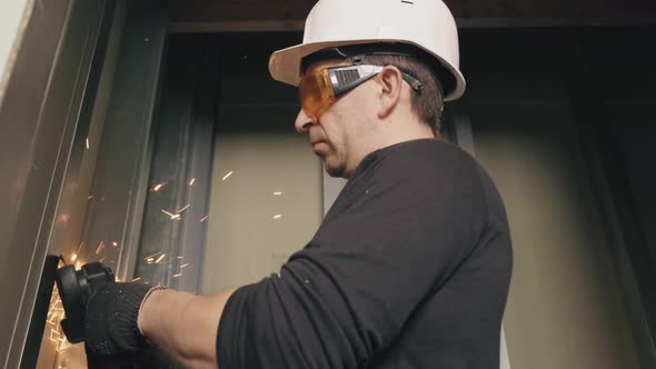 A Construction Worker in a Helmet and Glasses Works with an Angle Grinder