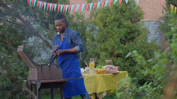 Focused Man in Apron Blowing Smoke on Barbecue Grill Outdoors