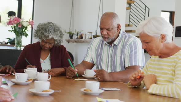 Happy senior diverse people drinking tea and playing bingo at retirement home