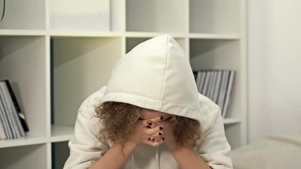 Teenage Girl Sits Alone and Cries Covering Her Face with Her Hands