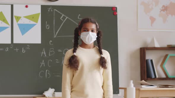 Black Schoolgirl in Face Mask Standing in Classroom and Posing for Camera