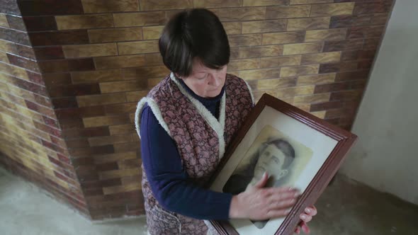 Elderly Woman Becoming Sad While Holding and Looking at Old Photo Portrait of Ancestor