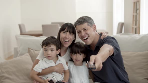 Happy Parents Couple with Two Kids Watching Favorite Show