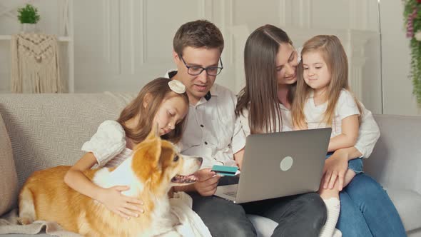 A Happy Family Uses a Laptop for Online Shopping, Sitting on the Couch at Home.