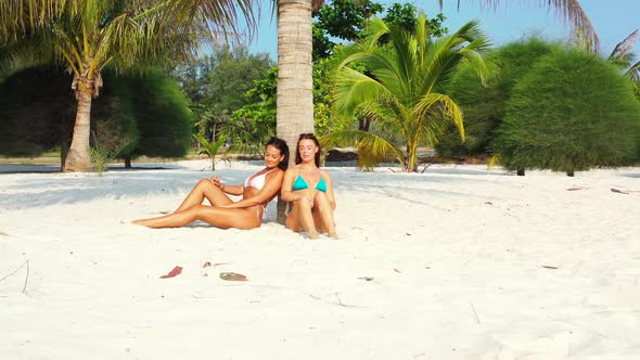 Pretty happy ladies on photoshoot by the sea on beach on sunny blue and white sand background 