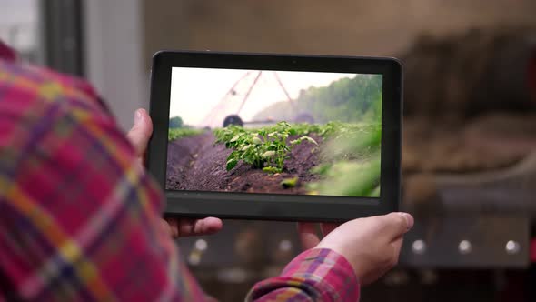 Close-up, Farmer Holds Digital Tablet in Hands on Background of Potato Storage Warehouse. It Shows