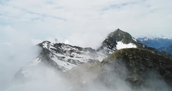 Forward Aerial Top View Over Cloudy Rocky Snowy Mountain in Sunny Day with Clouds