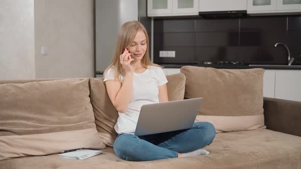 Woman Talking on Mobile While Sitting on Sofa with Laptop