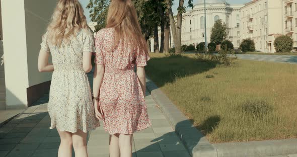 Two young beautiful smiling hipster girls in trendy summer sundress posing outdoors