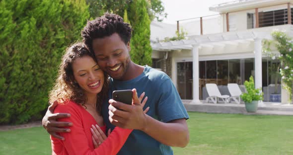 Happy biracial couple taking selfie in garden after proposal