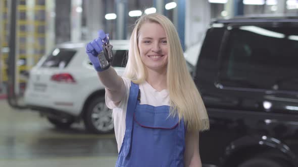 Portrait of Smiling Blond Caucasian Woman Showing Car Keys To Camera. Young Female Auto Mechanic