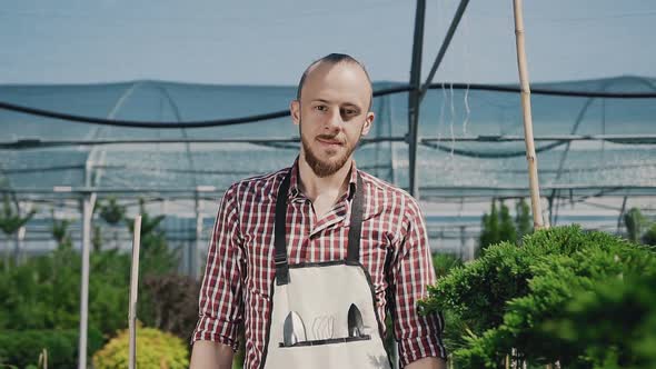 Young Guy is a Gardener in Mittens and a Garden Apron, Smiling and Posing 