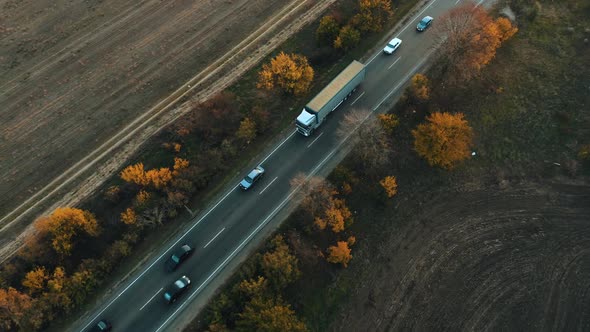 Aerial View of a Truck Driving in a Flow of Cars Along the Highway at Autumn Sunset