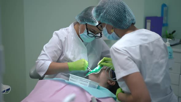 Focused Female Orthodontist Curing Ill Tooth of Patient in Dental Chair with Assistant Removing