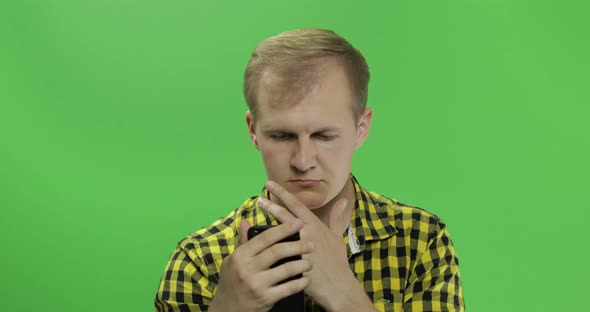Caucasian Man in Yellow Shirt Scrolling, Texting on the Smartphone in His Hands
