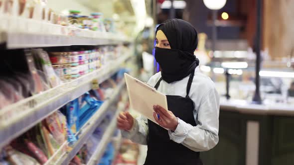 Woman in Black Scarf Working in Store Inspecting Shelves with Tablet