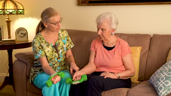 Home healthcare therapist helping elderly woman with physical therapy with hand weights.