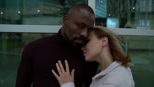 an African Man in Dark Clothing and a Blonde Woman in a Gray Jacket Are Hugging Each Other and
