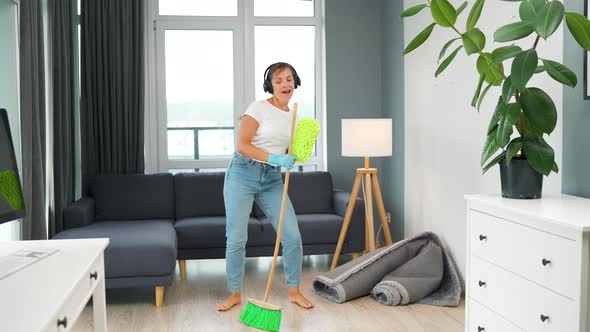 Woman in Headphones Cleaning the House and Having Fun Dancing with a Broom and Washcloth