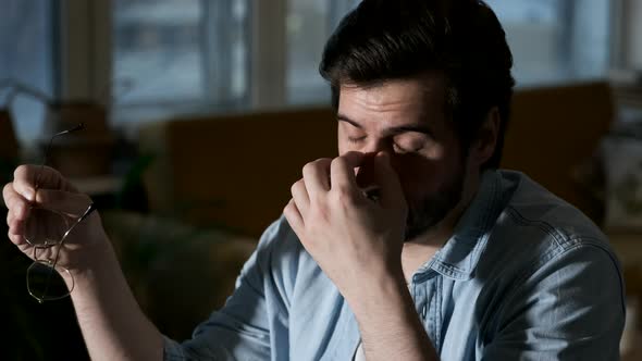 Young Tired Man Takes off his Glasses, Works Using laptop Online in a Dark Room at Home