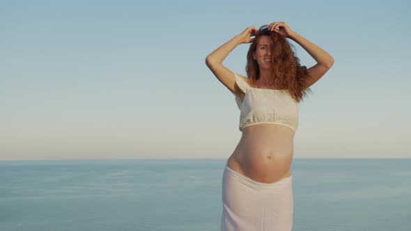 Pregnancy Woman Dancing Emotionally Having Fun on the Street Against the Background of the Sea.