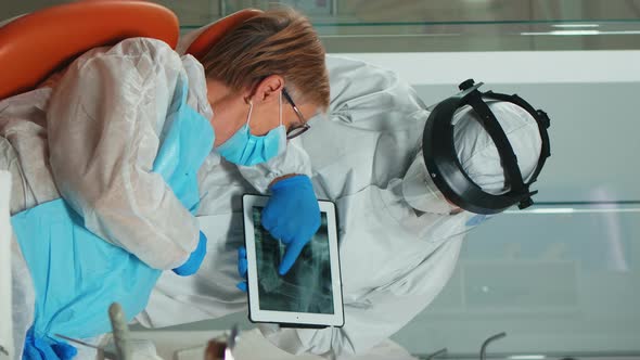 Vertical Video Stomatologist in Protective Suit Reviewing Xray of Tooth Using Tablet