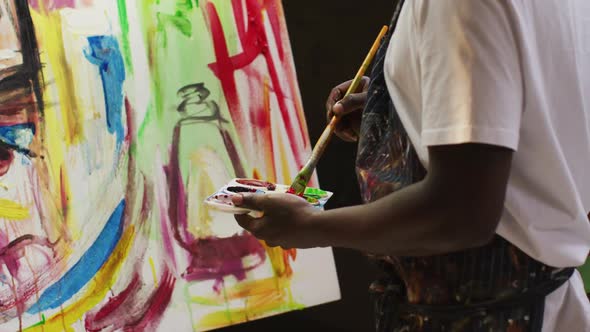 African american male artist wearing apron painting with paint brush on canvas at art studio