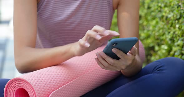 Woman use of mobile phone with her yoga mat at outdoor