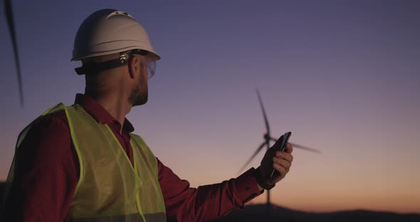 Engineer Browses Information on the Phone Standing on the Background of Windmills Looking Away To