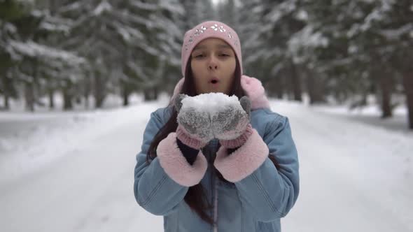 The Girl Blows Snow From Her Hands and Smiles While Standing in the Winter Forest on the Background