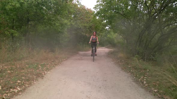 Aerial Slow Motion Shot of Young Sport Woman Rides Bicycle on Countryside Dusty Road at Summer