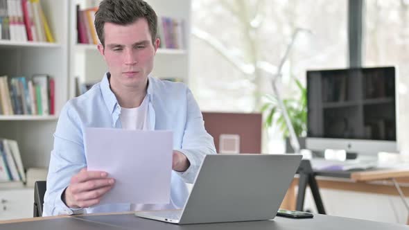 Reading Document By Young Man and Working on Laptop