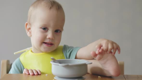 Naughty Baby Child Putting Foot Leg on Table While Eating Having Lunch in Kitchen