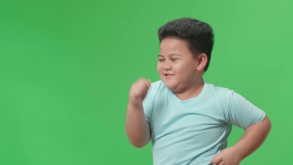 Side View Of Smiling Asian Little Boy Dancing In A Green Screen Studio alt