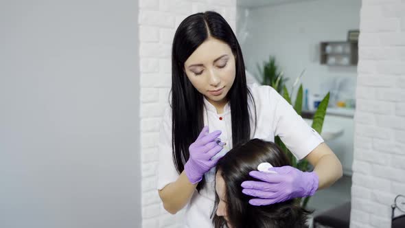 A young beautician makes injections into the head's skin of a woman to restore